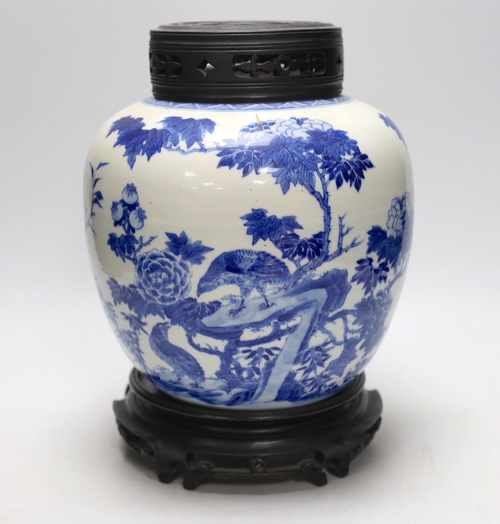 A large Chinese blue and white porcelain jar, 19th century decorated with scenes of birds amongst foliage with associated pierced hardwood cover and stand, 29cms high including stand and cover